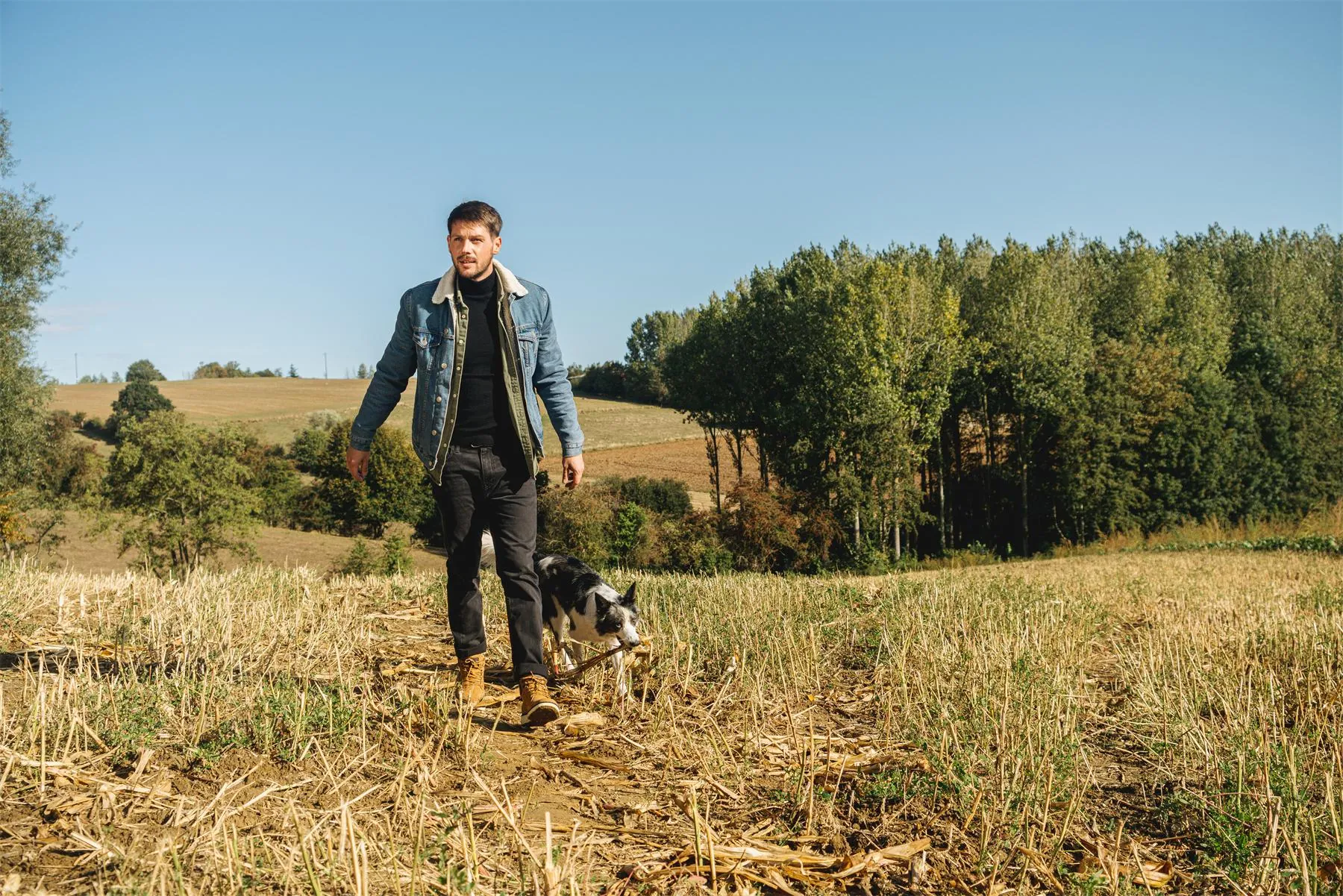 Homme en veste en jean marchant dans un champ avec son chien, chaussures de ville Chaussexpo