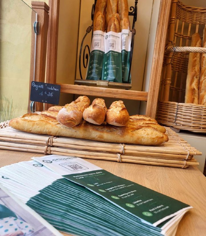 Sacs à pain et dépliants Groupama posés devant les baguettes d'une boulangerie locale
